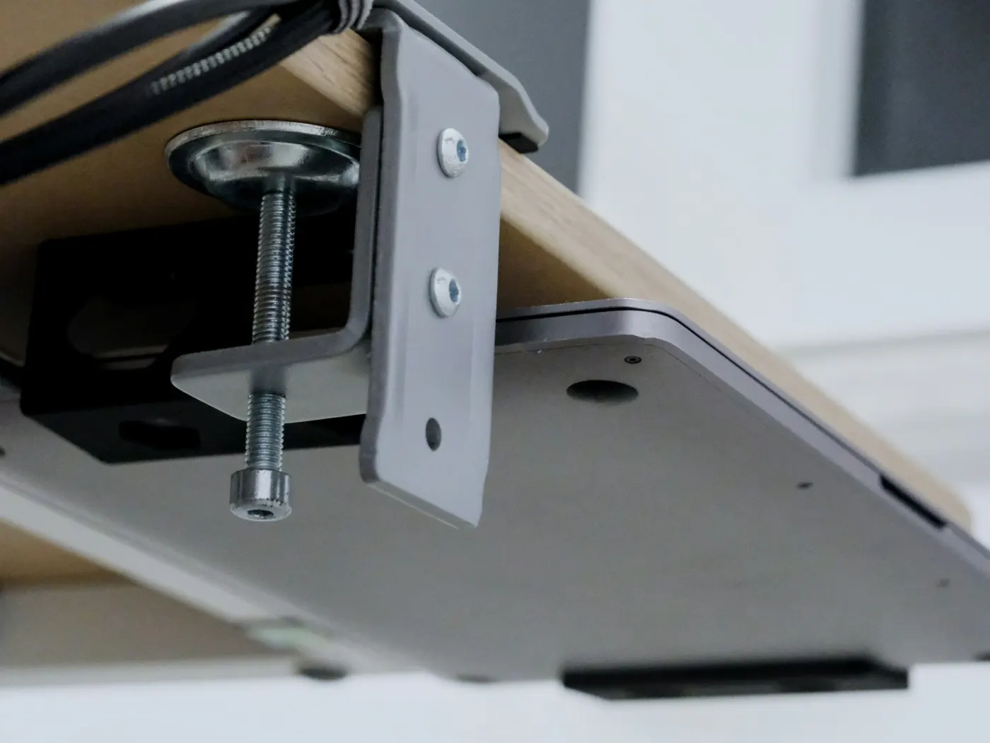 A laptop clamped under a wooden desk with its cables tidied
